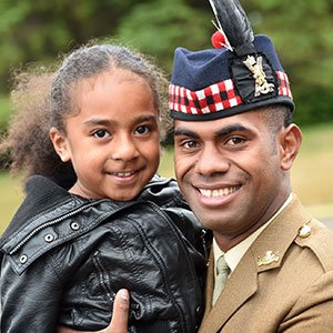 Army dad in dress uniform hugging his daughter and smiling at camera