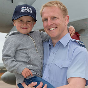 Airforce father holding his small child who is wearing a Royal Air Force baseball cap