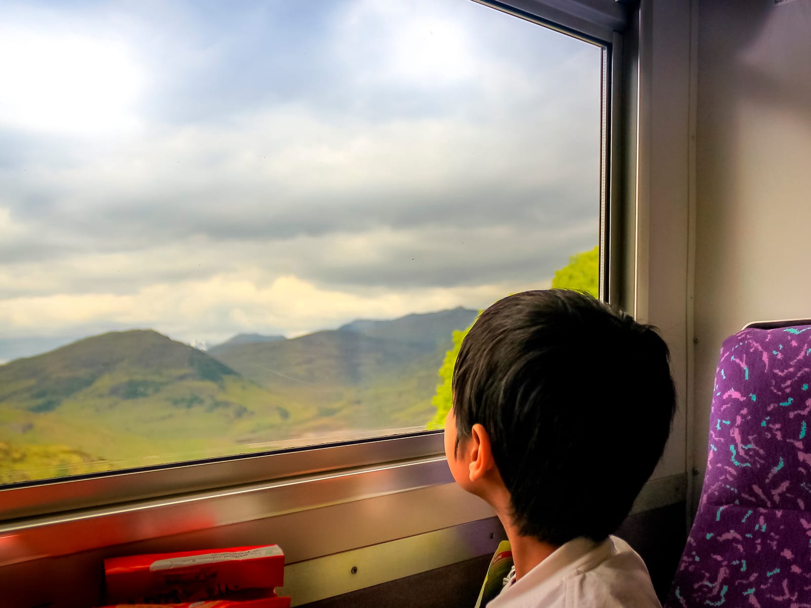 Young child looking out of a train window at the Scottish country side