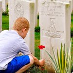 A young kid leaving a poppy in front of a remembrance grave