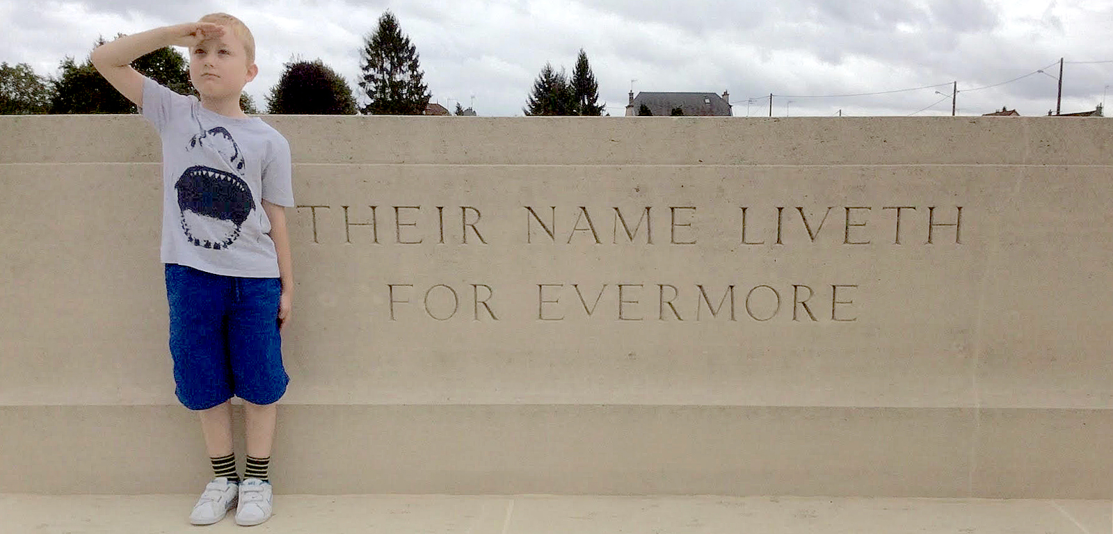 Young child saluting in front of a memorial stone with the inscription "Their names live for evermore"
