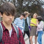Teenage boy looking sad while classmates talk behind his back