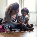 A mother sitting on the floor talking to her little girl who has a pink bow in her hair