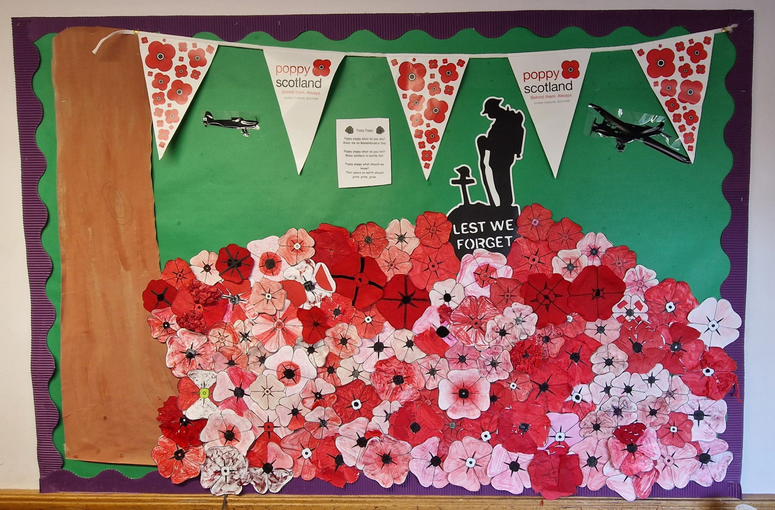 A wall display shows a colourful mountain of hand drawn poppies with a "lest we forget" memorial graphic