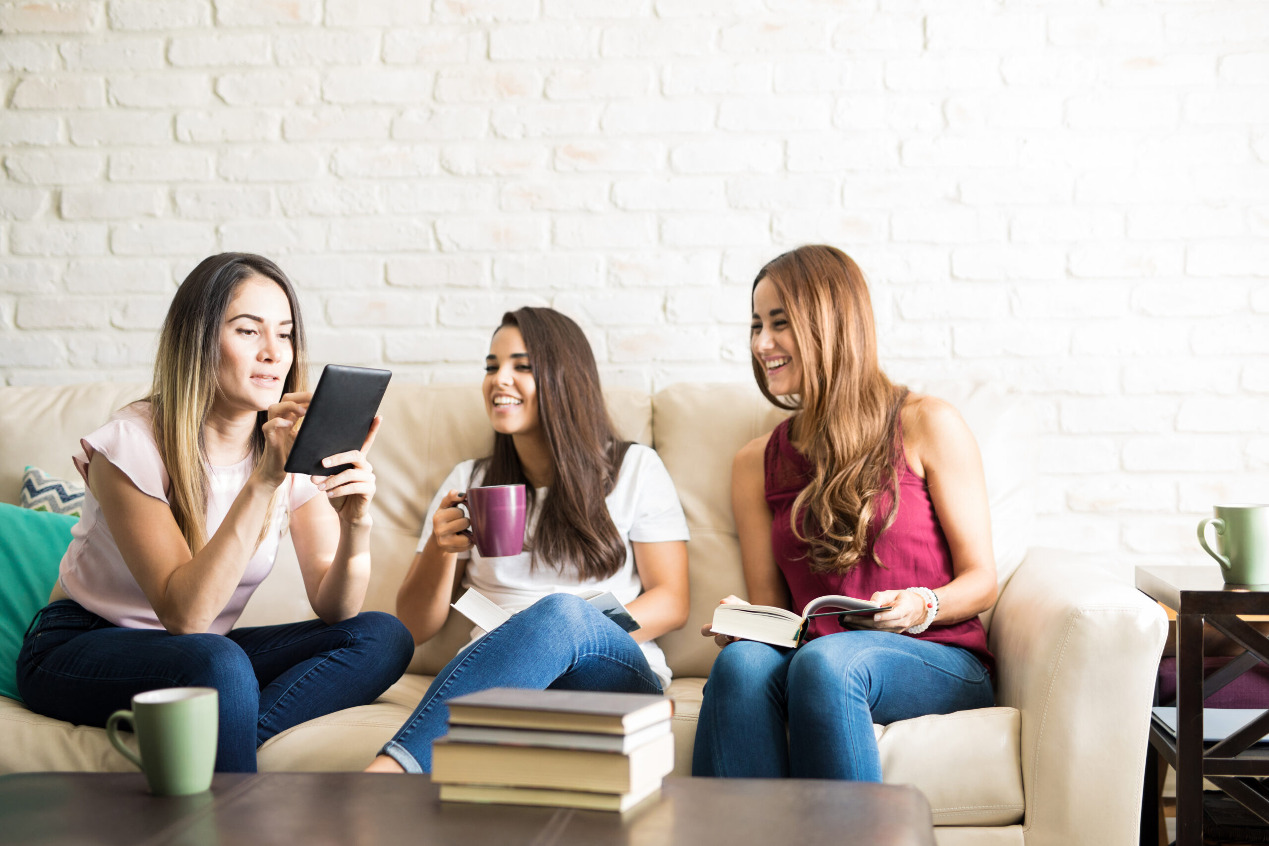 Three women sit on a sofa discussing the book they are currently reading.