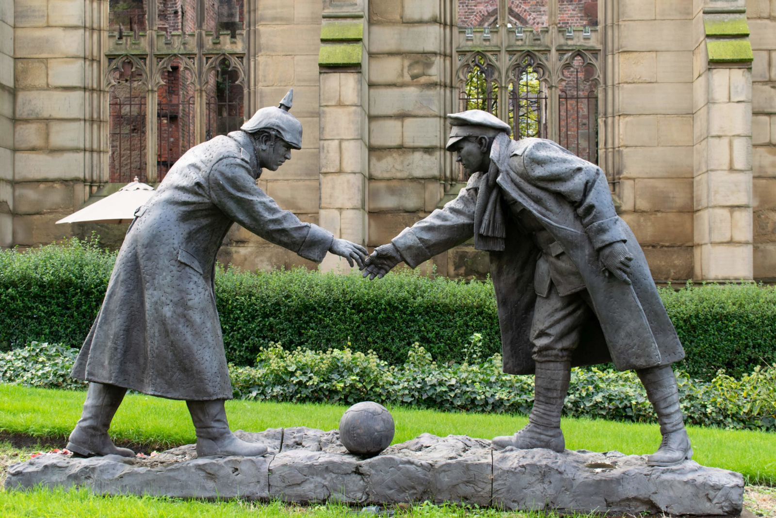 A bronze war memorial shows two soldiers shaking hands over a football on the ground.