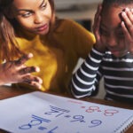 A teacher sits with a struggling pupil working on maths problems.