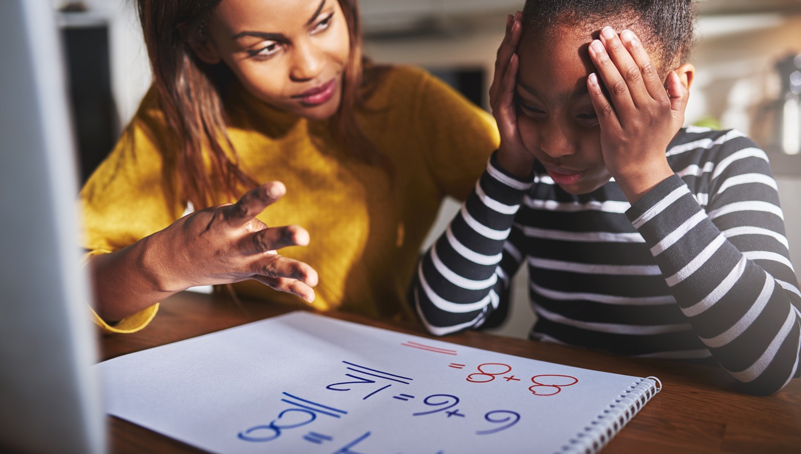 A teacher sits with a struggling pupil working on maths problems.