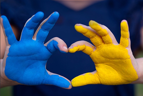 A child makes a heart shape with their hands, one covered in blue and one in yellow paint, symbolising the Ukrainian flag.