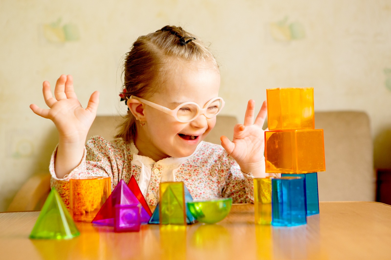 A young girl with Down's syndrome is delighted by a tower of transparent orange and blue building blocks.