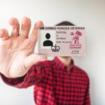 A veterans card is held to camera obscuring the holder's face. The person is wearing a red and black checked shirt.