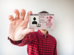 A veterans card is held to camera obscuring the holder's face. The person is wearing a red and black checked shirt.