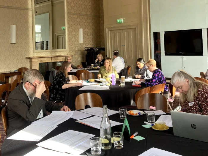 Attendees at large round tables covered in black cloth read papers.