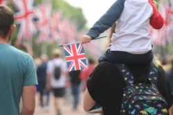 A child sits on someone's shoulder holding a Union Jack flag, as they walk down a flag lined street.