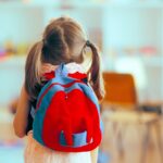 A little girl wearing a backpack enters an empty classroom.