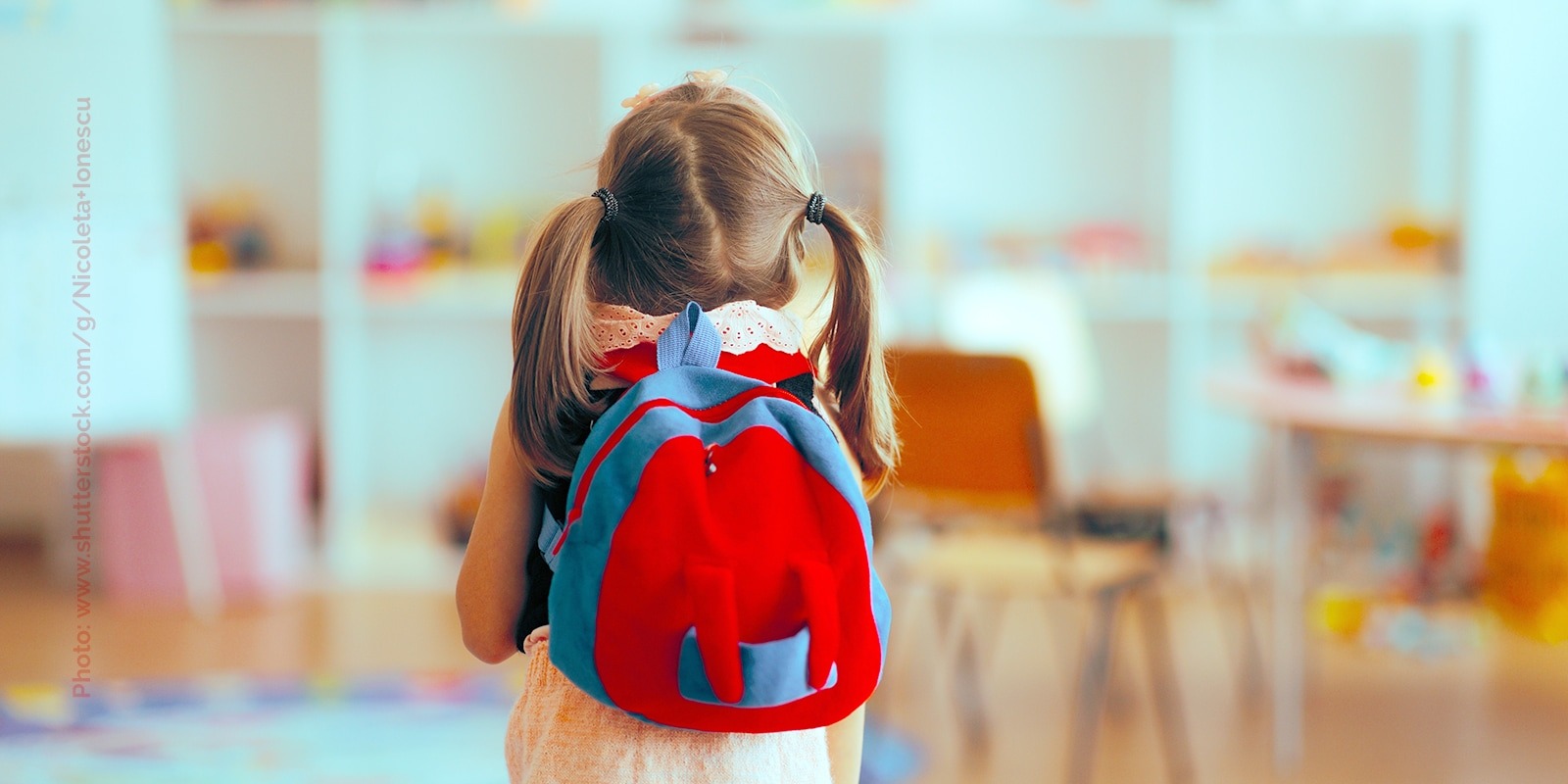A little girl wearing a backpack enters an empty classroom.