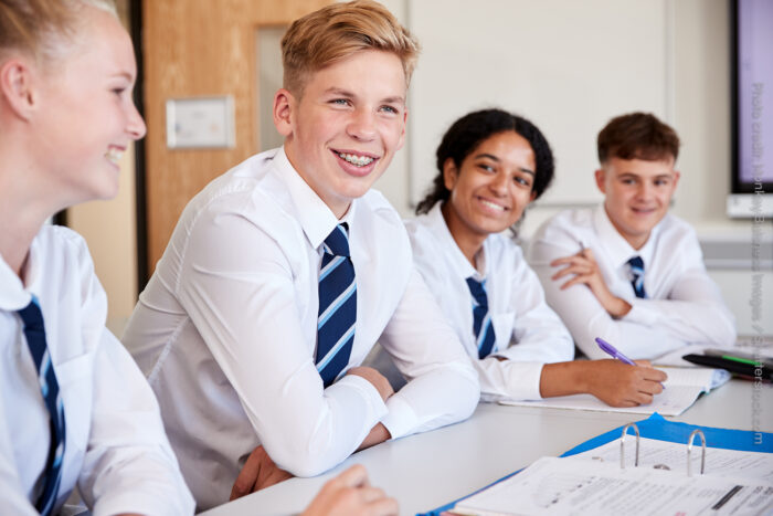 A group of four secondary students work on a project at a desk in a classroom.